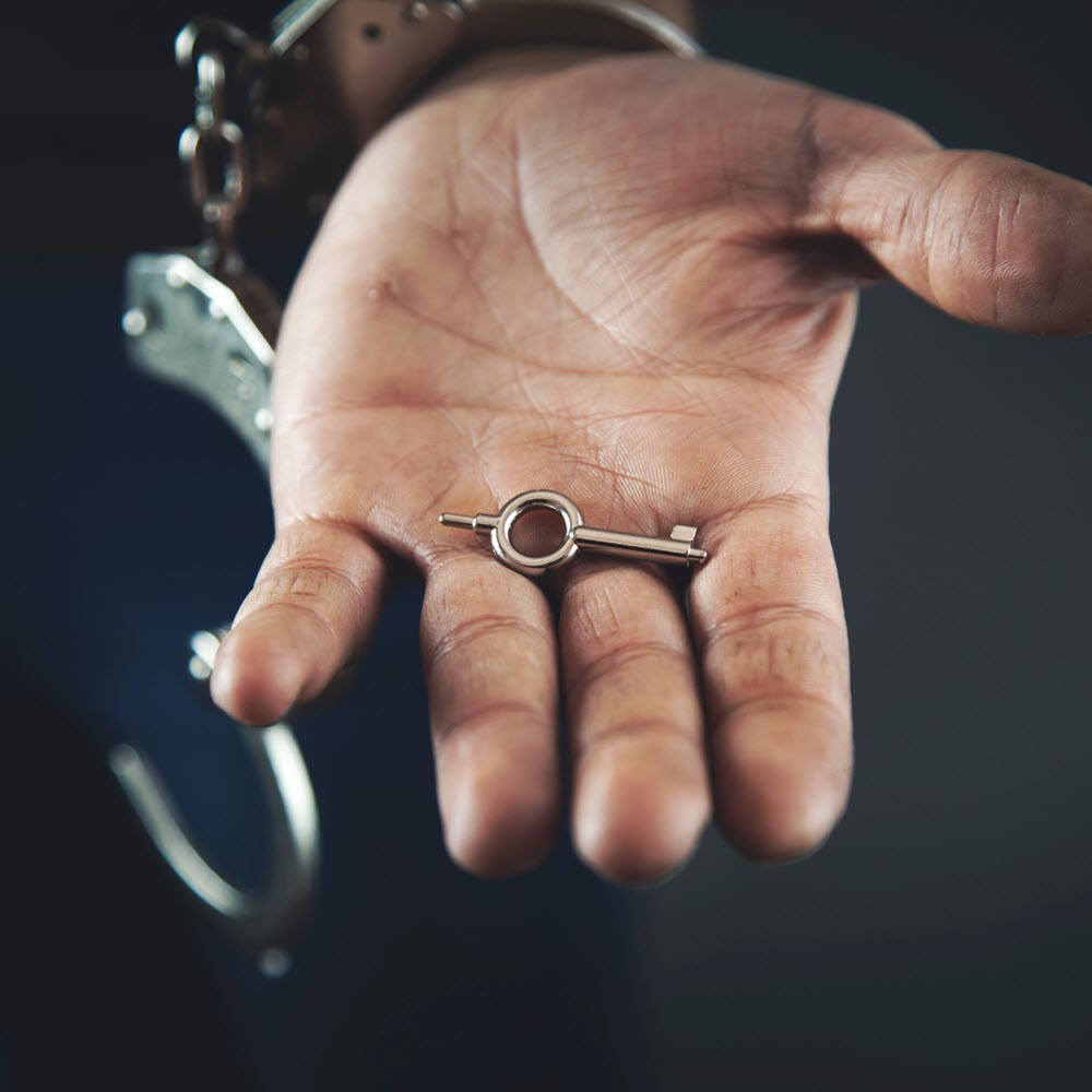 Hand with unlocked handcuffs holding key dark background 1000x1000.jpg