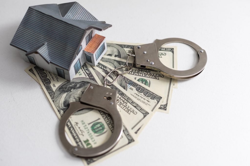 A small house lies on a fan of hundred dollar bills. The keys to the purchased house. Reduced copy of the house on a white background.