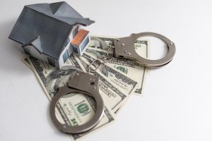 A small house lies on a fan of hundred dollar bills. The keys to the purchased house. Reduced copy of the house on a white background.