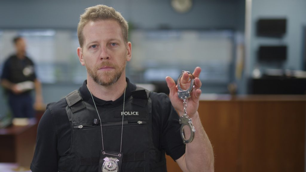 Caucasian police officer holding up handcuffs.