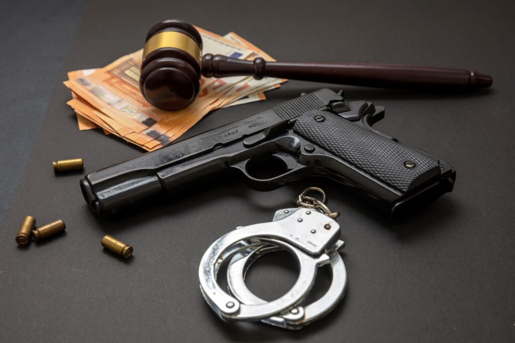 Handgun beside a stack of cash handcuffs and a gavel on a dark surface implying crime and legal action